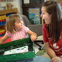 Teacher with young child looking amused and holding an art project.