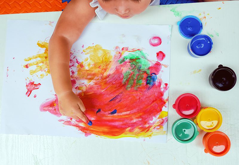 Young child finger-painting with colored paint on a poster in a learning center.